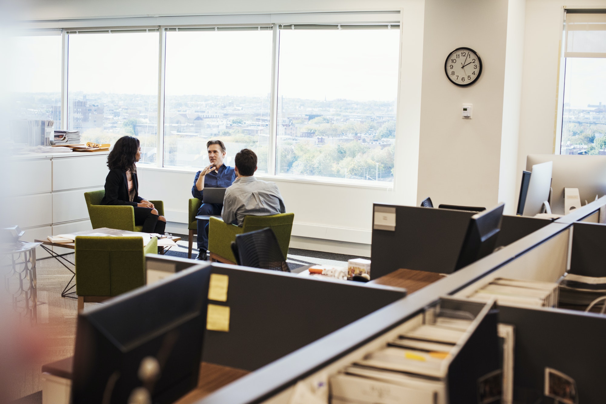 A woman and two men sitting in armchairs in an office talking to each other.